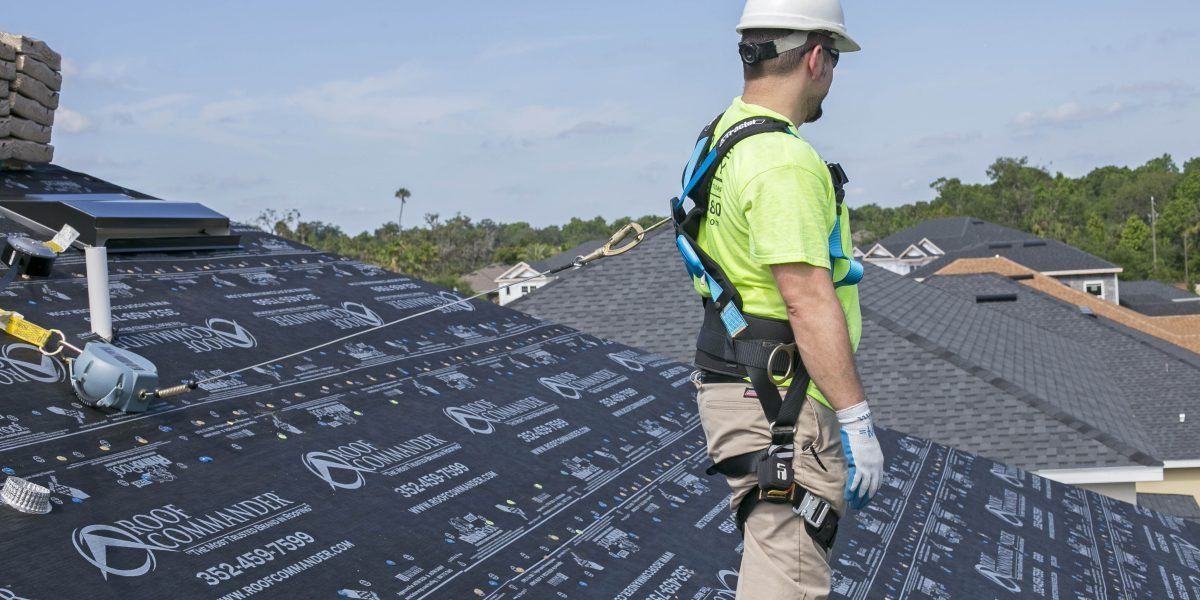A man wearing a hard hat and safety harness is standing on top of a roof.