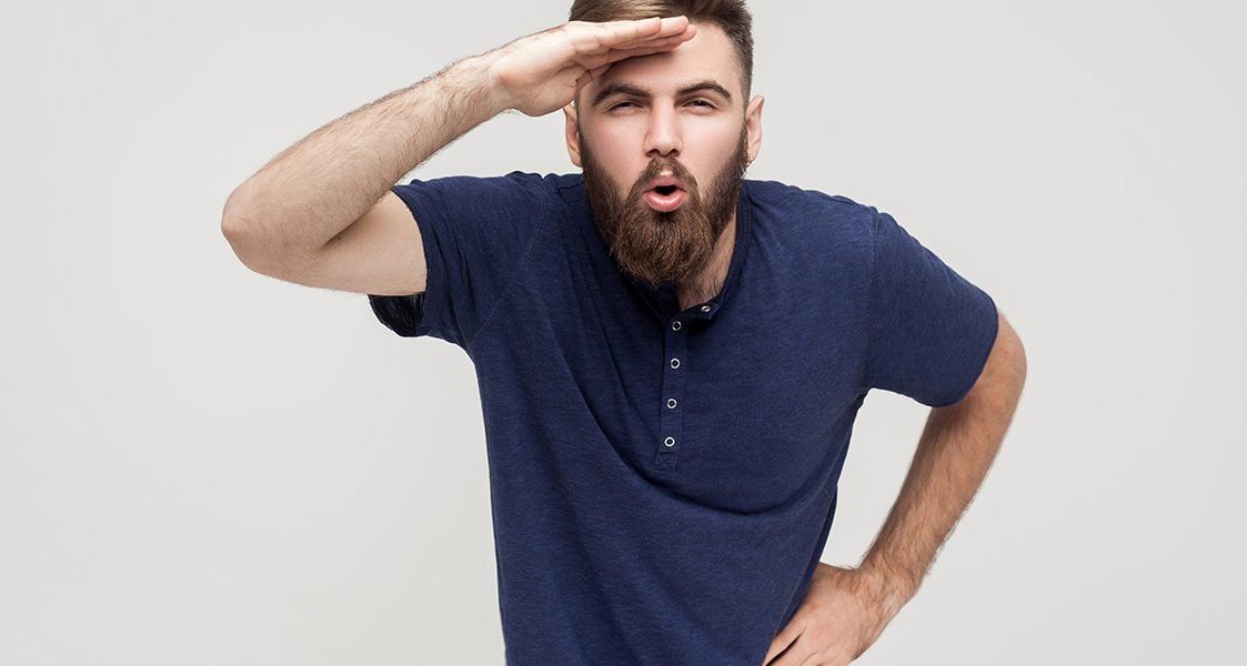 A man with a beard is covering his eyes with his hand.