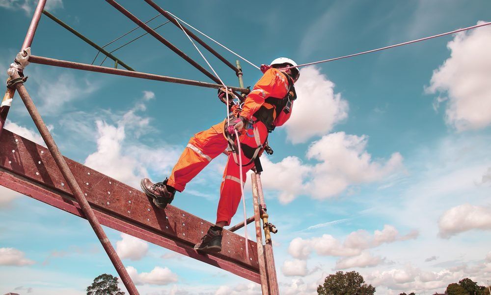 A man in an orange jumpsuit is climbing a scaffolding.