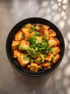 A bowl of mapo tofu with cubed tofu, a spicy red sauce, and topped with a generous amount of chopped green onions.