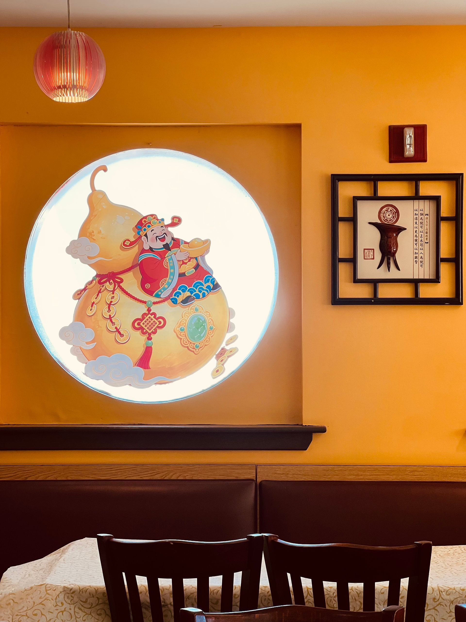 A circular mural of a stylized gourd featuring a figure in red, next to a framed calligraphic print on a yellow wall.