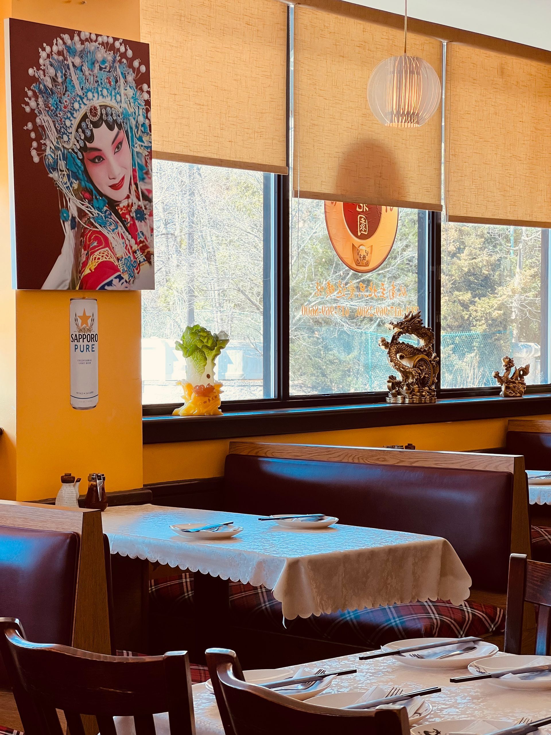 A bright restaurant corner featuring a large print of an opera performer, a booth table, and windows with neutral shades.