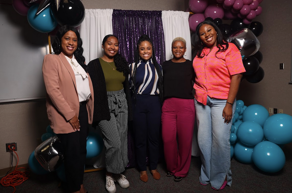 A group of women are posing for a picture in front of balloons.