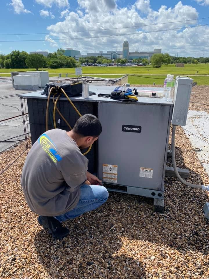 A man is working on an air conditioner on the roof of a building.