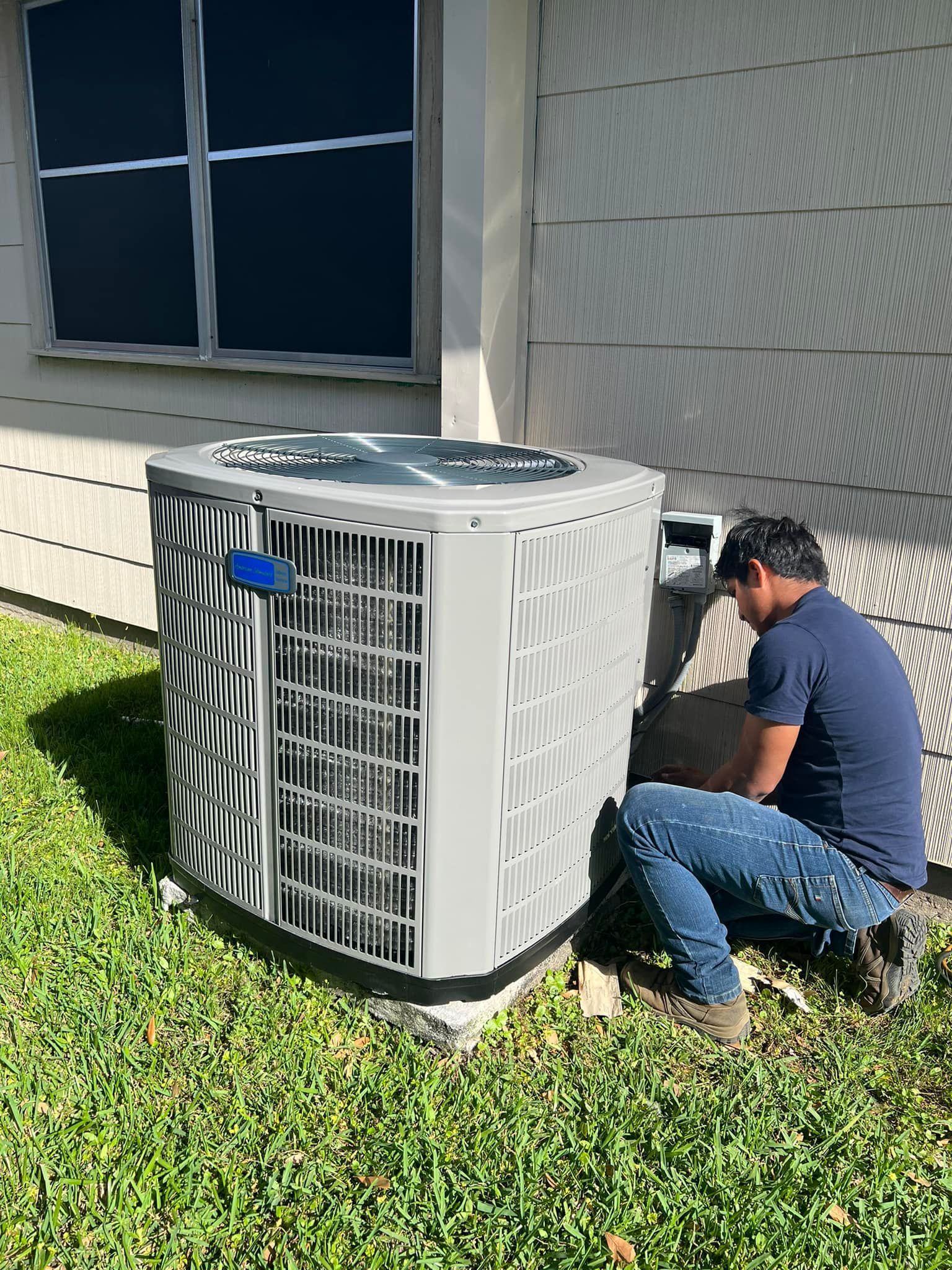 A man is kneeling down in front of an air conditioner.