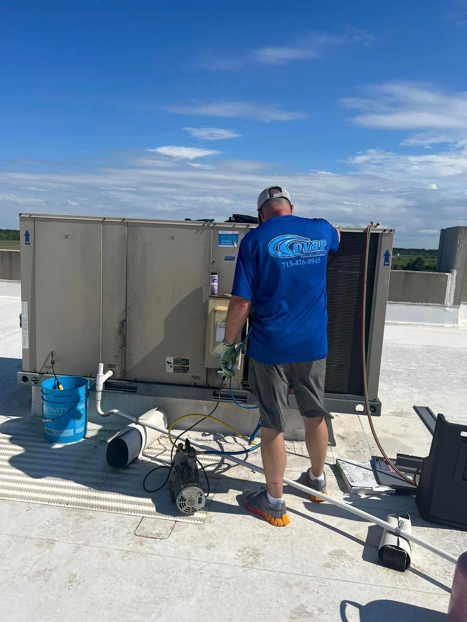 A man in a blue shirt is working on an air conditioner on a roof.