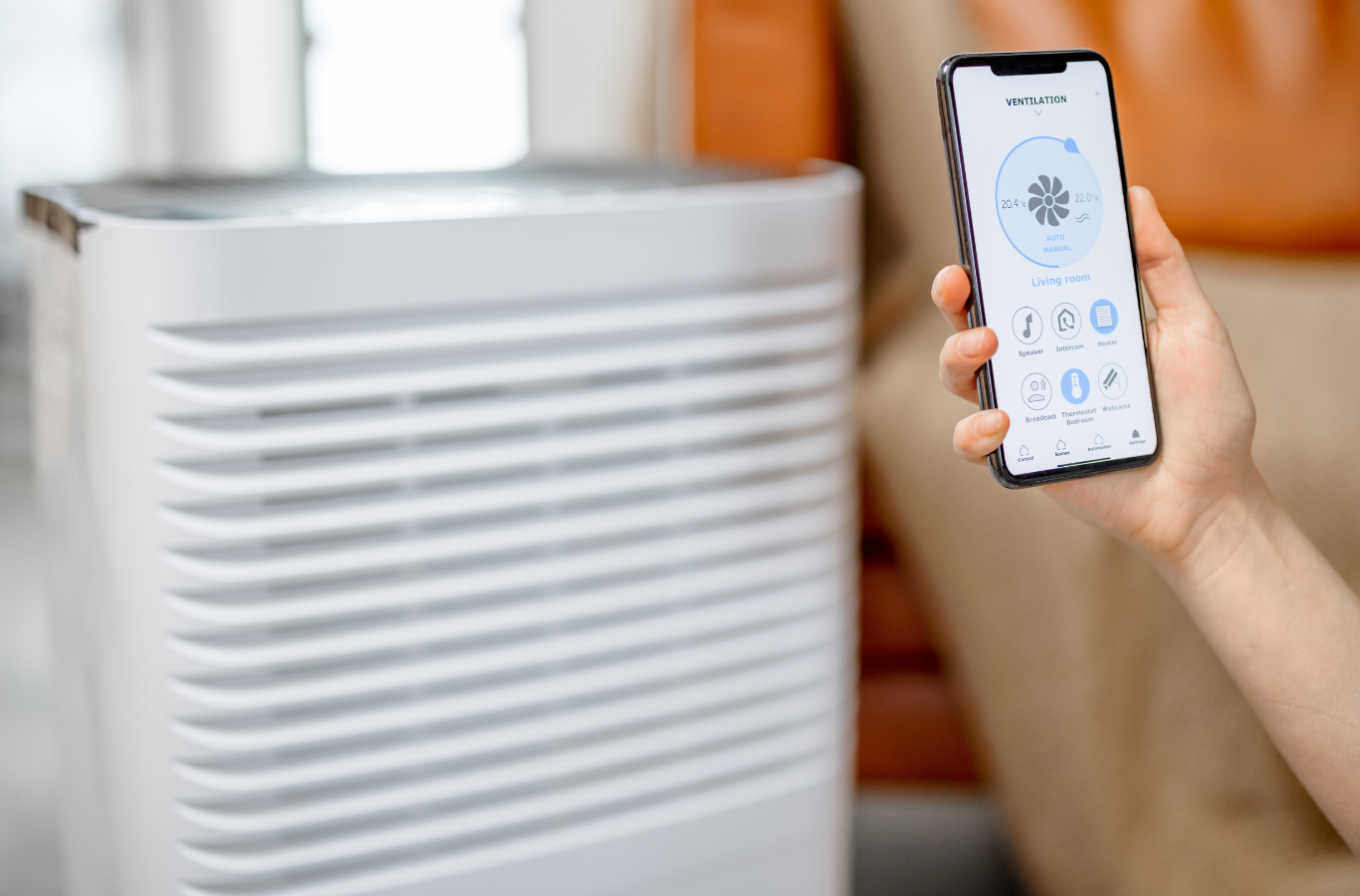 A person is holding a cell phone in front of an air purifier.