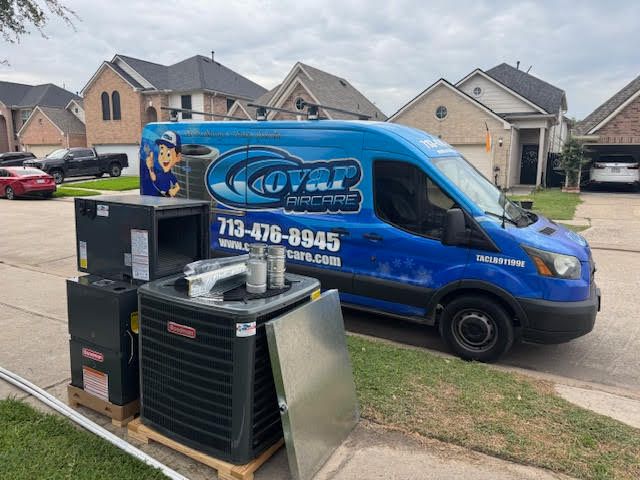 A blue van is parked in a driveway next to a stack of air conditioners.