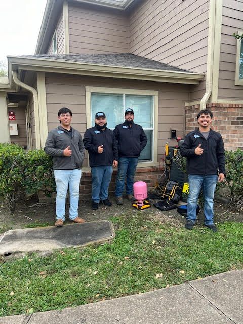 A group of men are standing in front of a house giving a thumbs up.