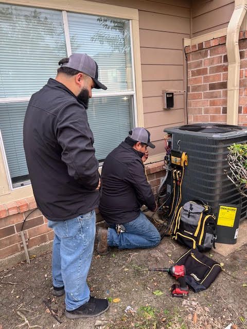 Two men are working on an air conditioner outside of a house.