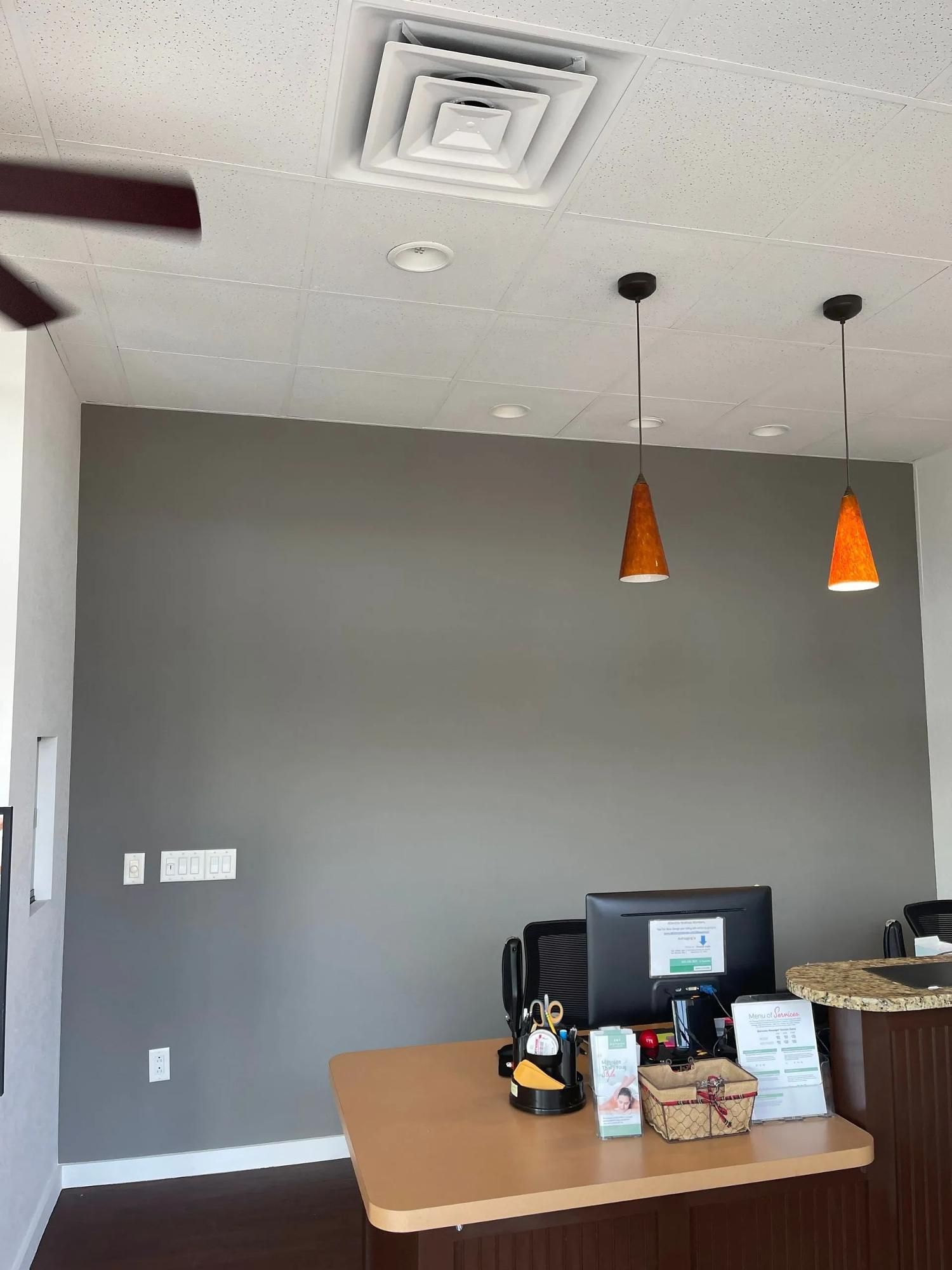 Empty gray office corner with a desk, computer, and two orange pendant lights