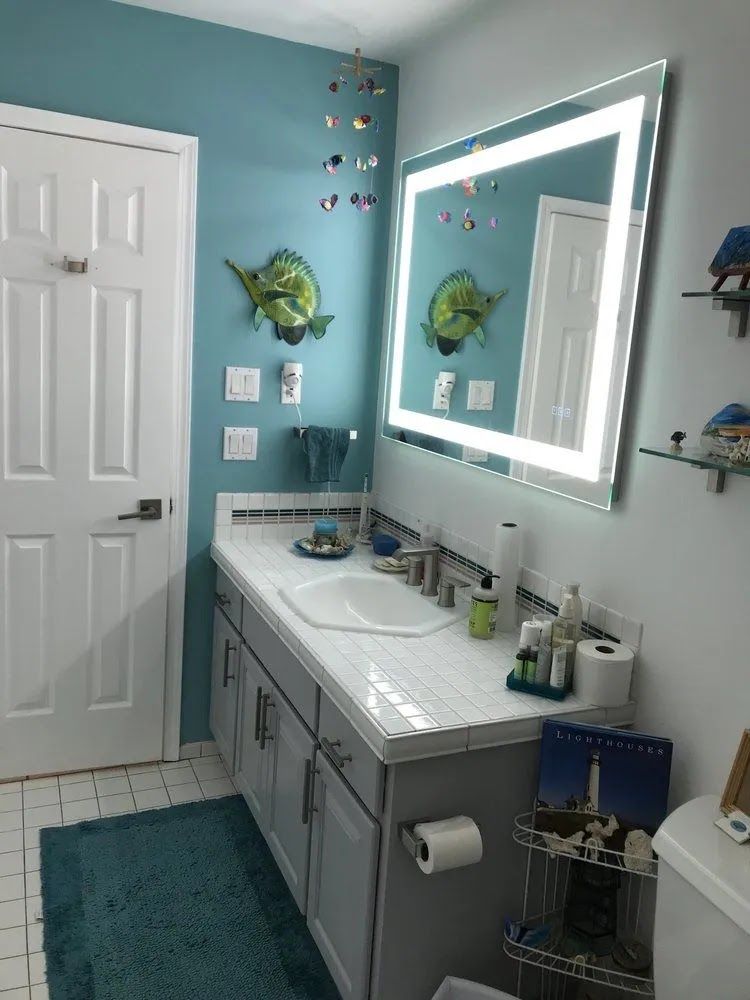 Bright turquoise bathroom with white vanity, lit mirror, teal rug, and wall decor.