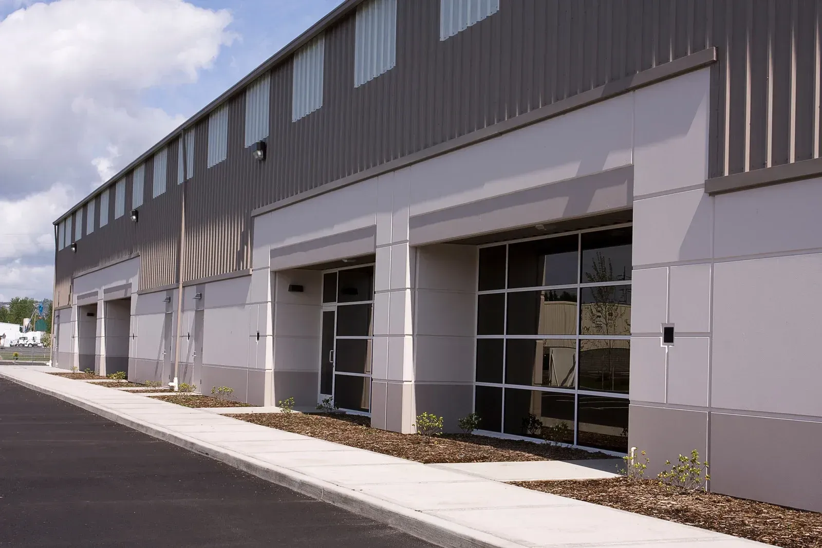 Modern industrial warehouse exterior with gray walls, glass garage doors, and a paved driveway