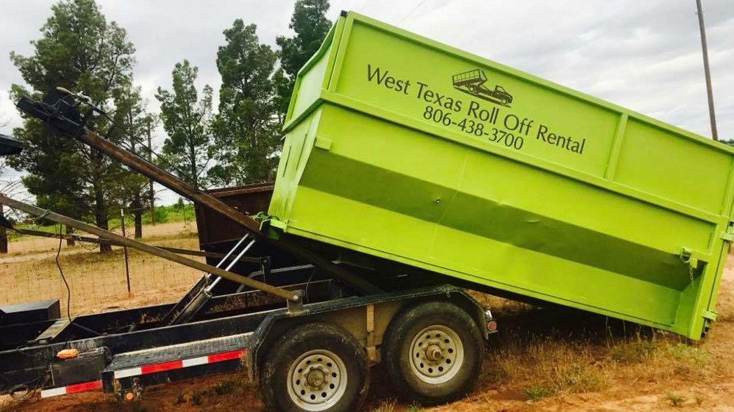 A green dumpster is sitting on top of a trailer in a field.