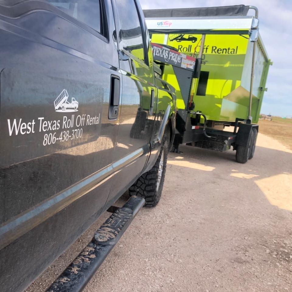A black truck is parked next to a green dumpster from west texas roll off rental