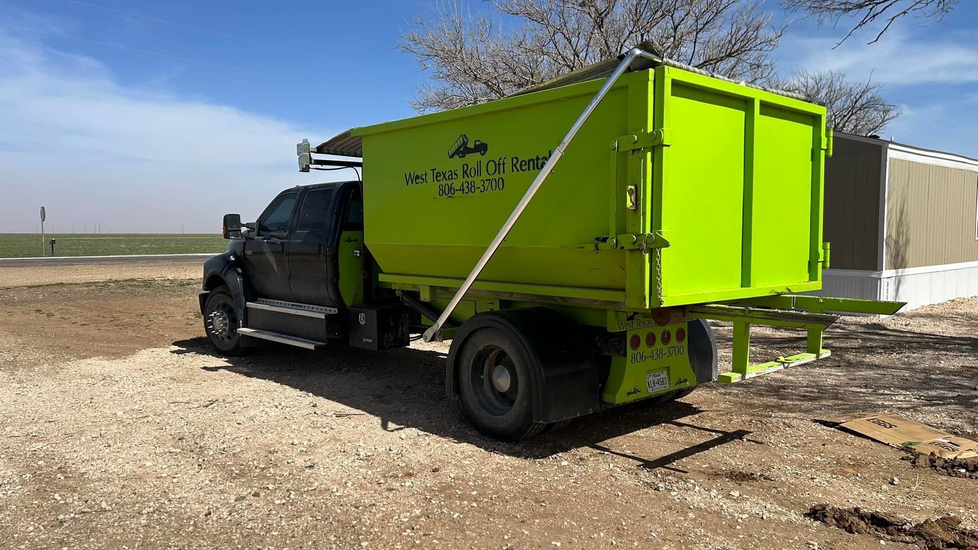 A green dumpster truck is parked in a dirt field.