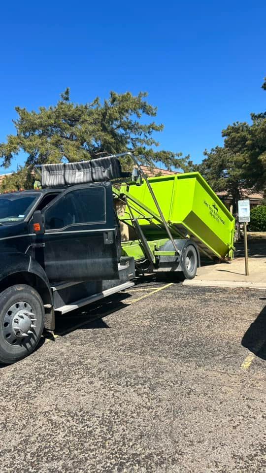 A dumpster is being towed by a truck in a parking lot.