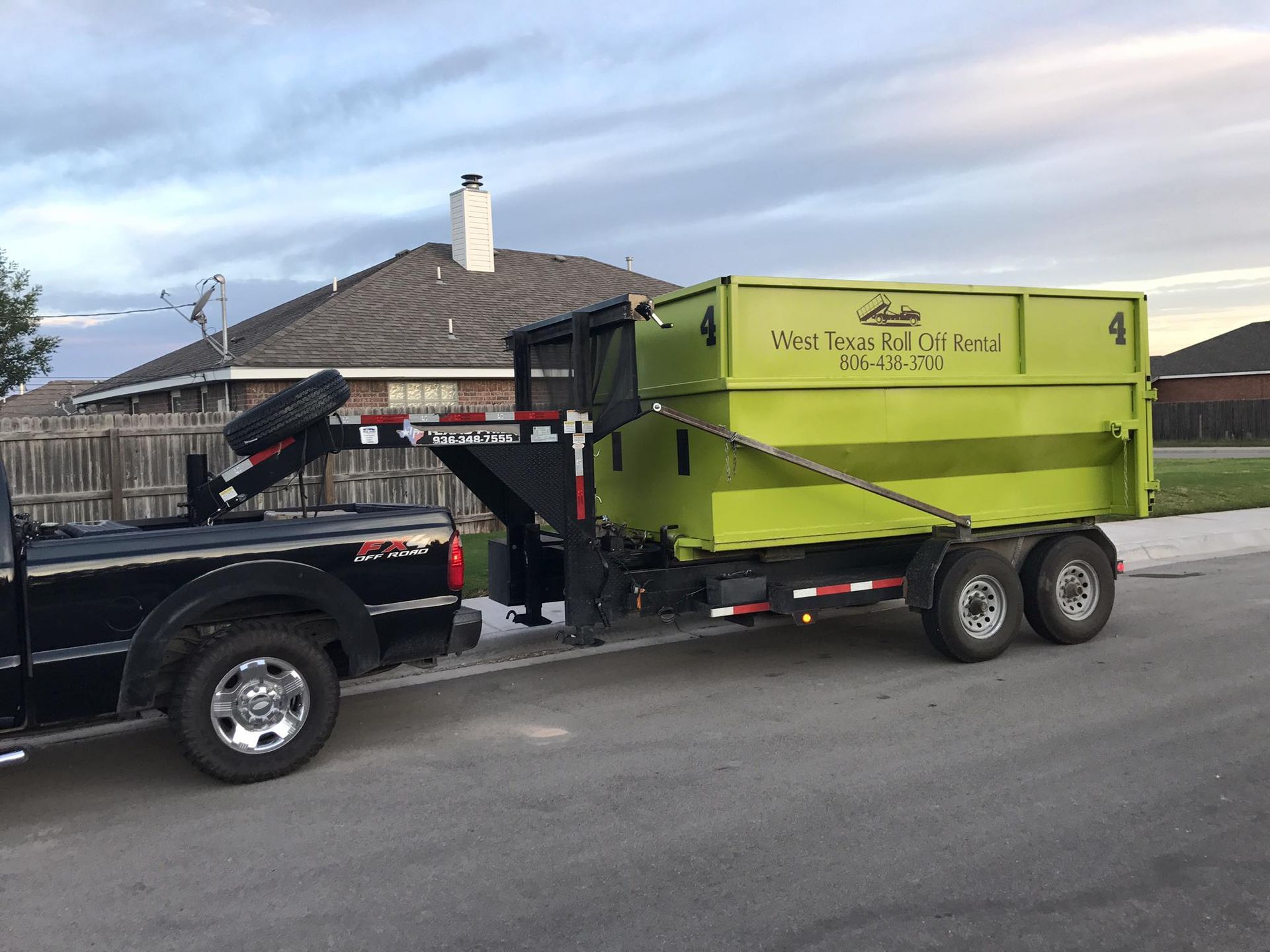A black truck is towing a green dumpster on a trailer.