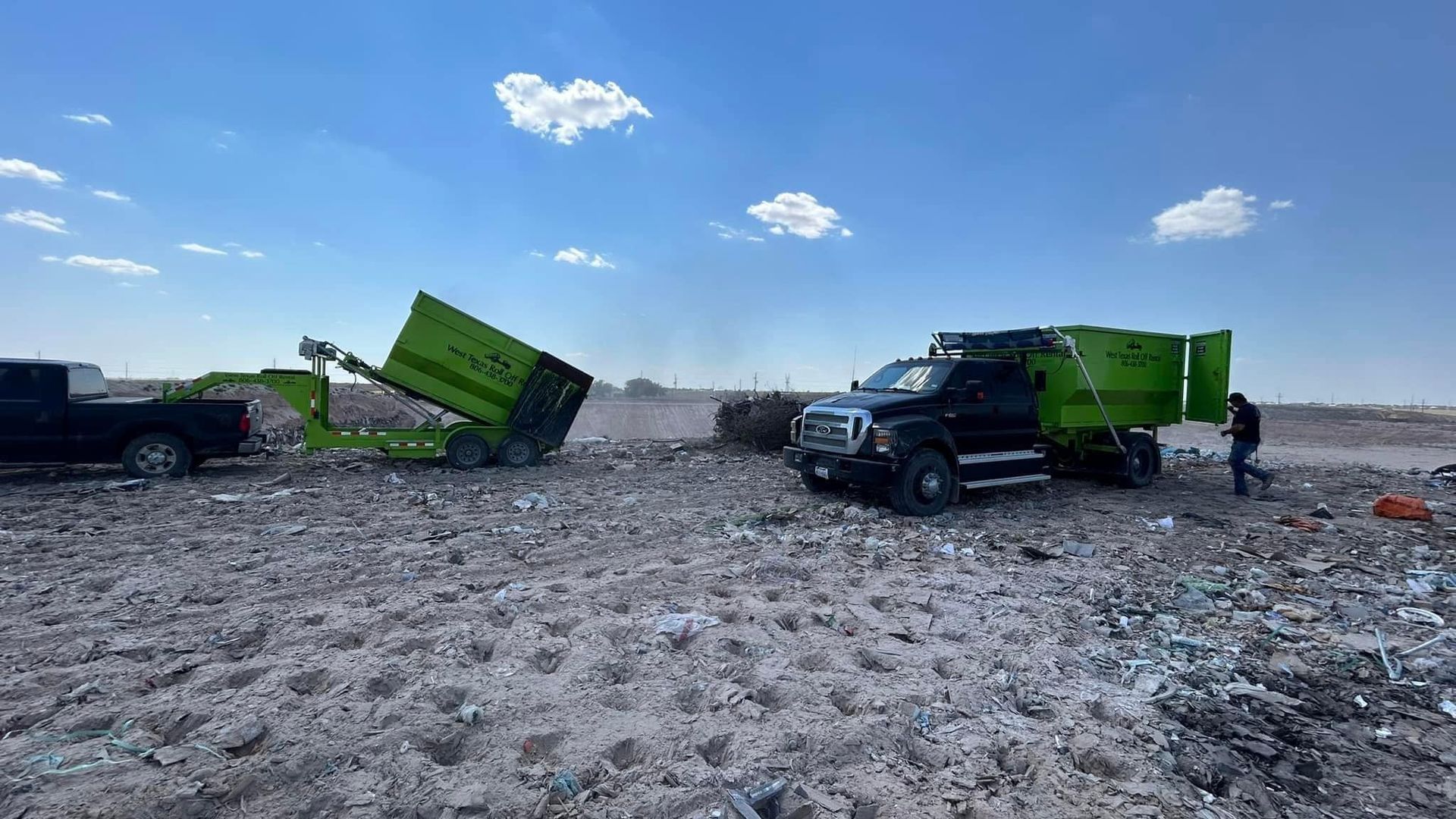 A garbage truck is sitting in the middle of a dirt field.
