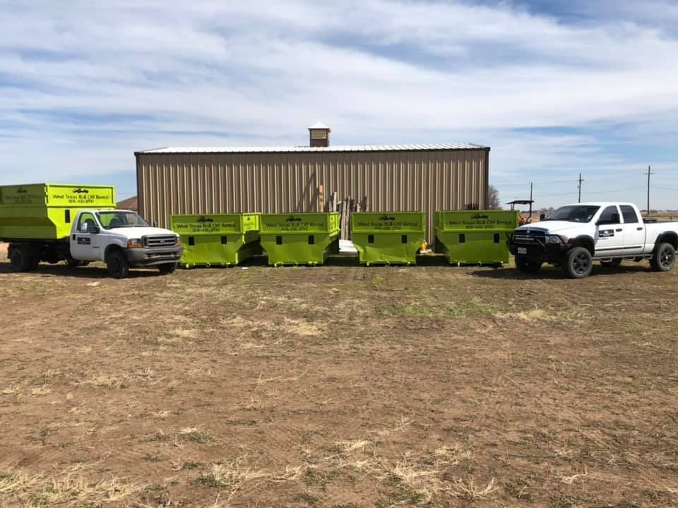 A row of dumpsters are parked in a field in front of a building.