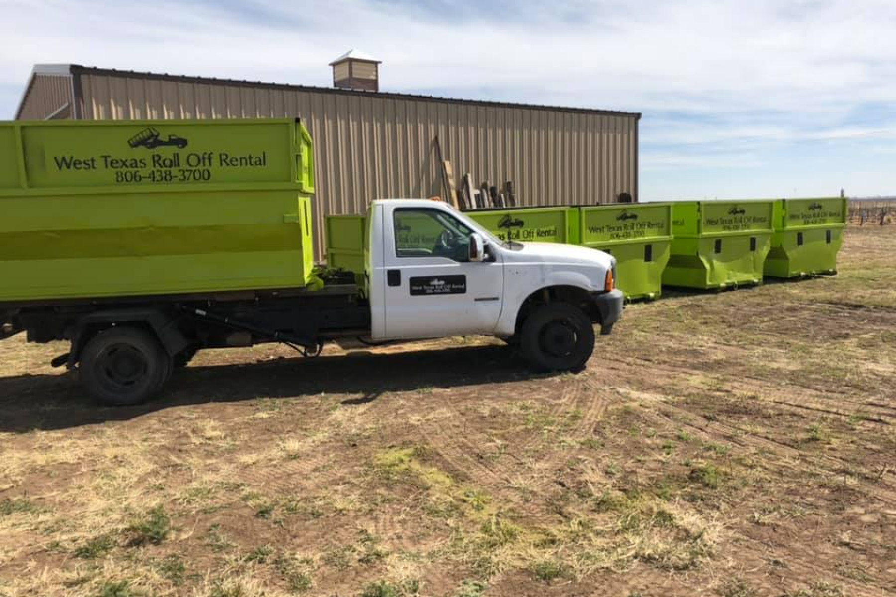 A dump truck is parked in a field next to a building.