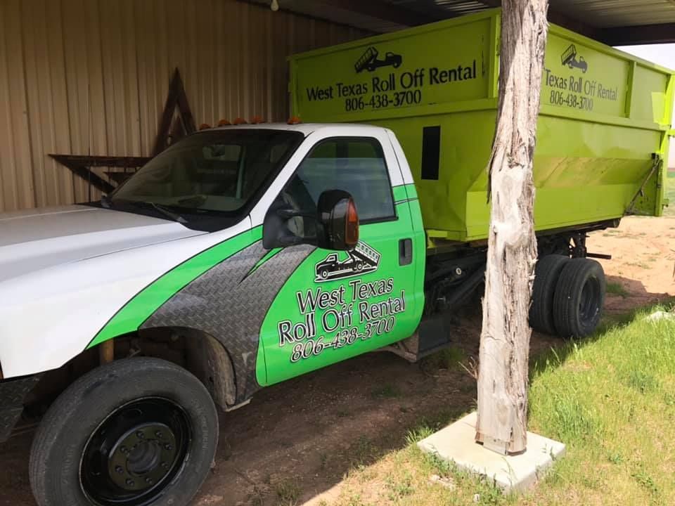 A green and white dump truck is parked in front of a building.
