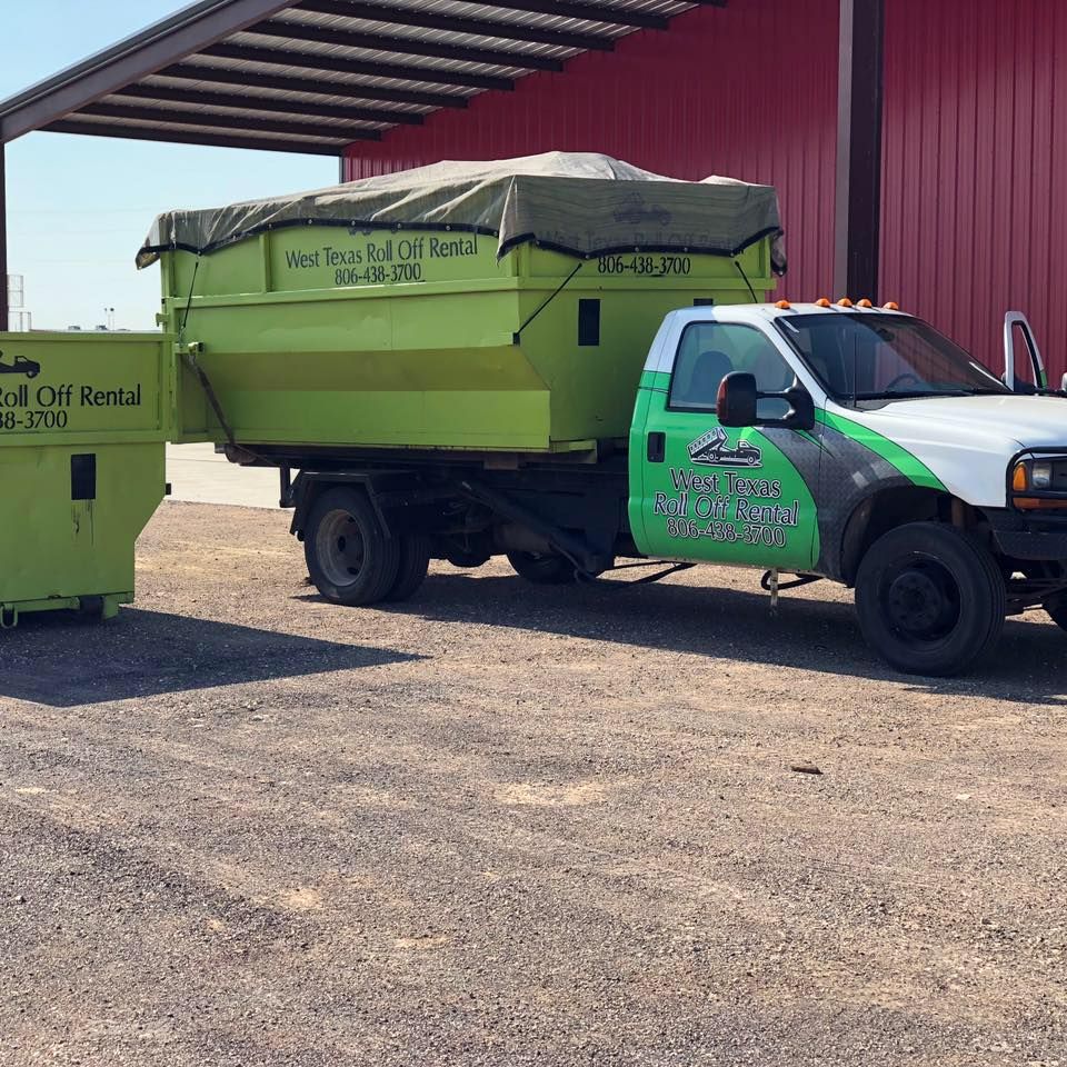 A green dump truck is parked in front of a red building