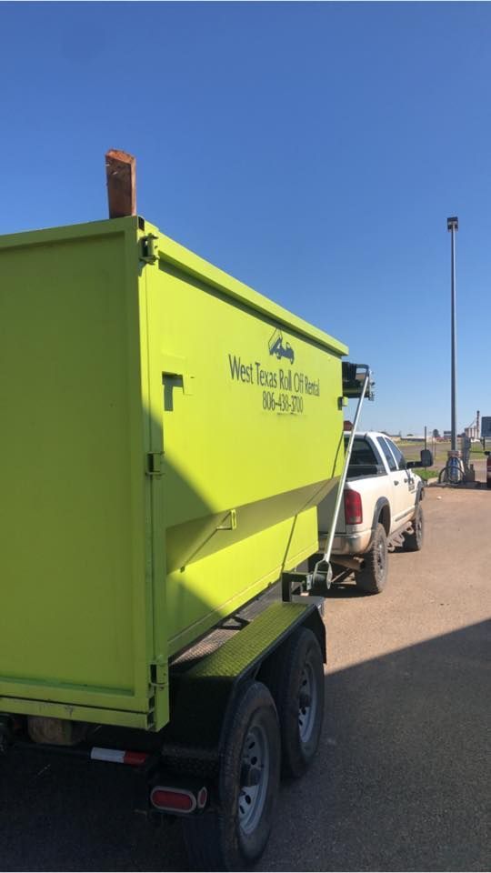 A yellow dumpster is parked next to a white truck