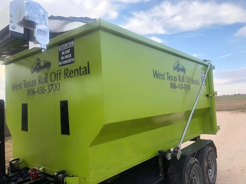 A green dumpster is parked in a dirt field.