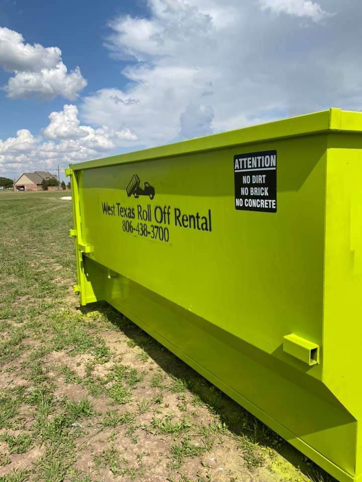 A yellow dumpster is sitting in the middle of a grassy field.