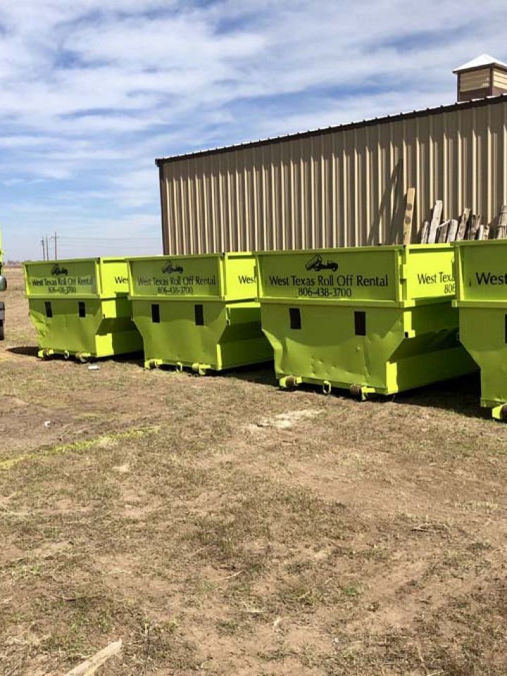 A row of green dumpsters are parked in front of a building.