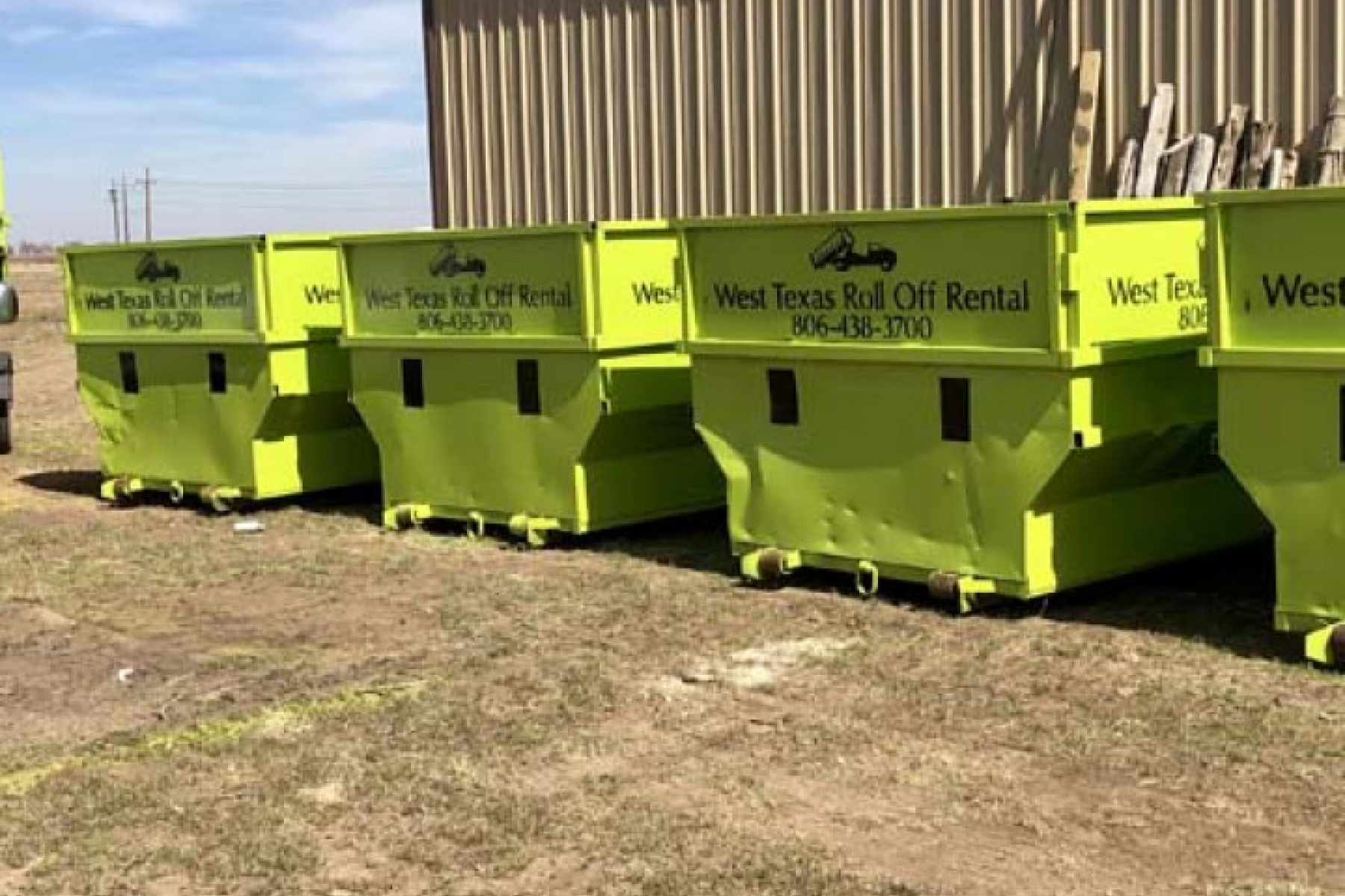 A row of green dumpsters are lined up in front of a building.