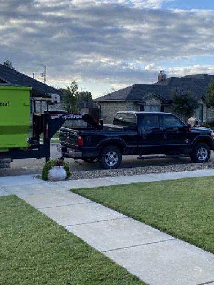 A black truck is parked in a driveway next to a green dumpster.