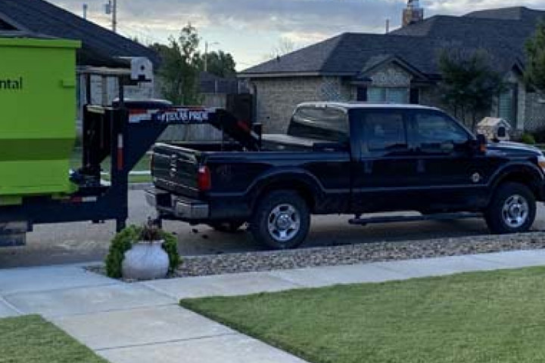 A black truck is parked in front of a house with a green trailer attached to it.