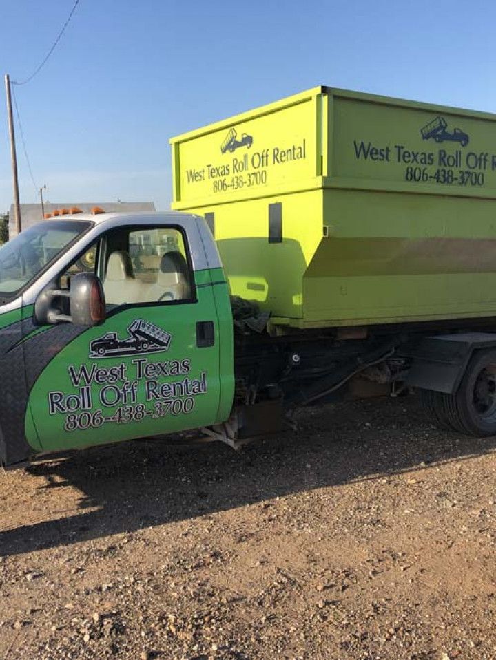 A green dump truck is parked next to a yellow dumpster.