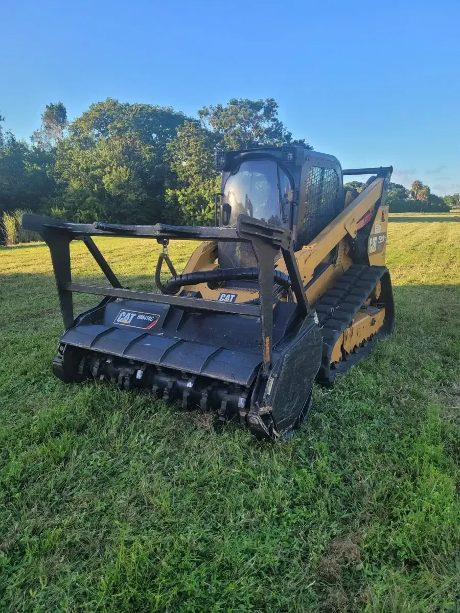 Yellow and black Caterpillar forestry mulcher on tracks, in a grassy field.