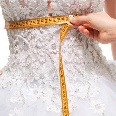 A woman in a wedding dress is measuring her waist with a tape measure