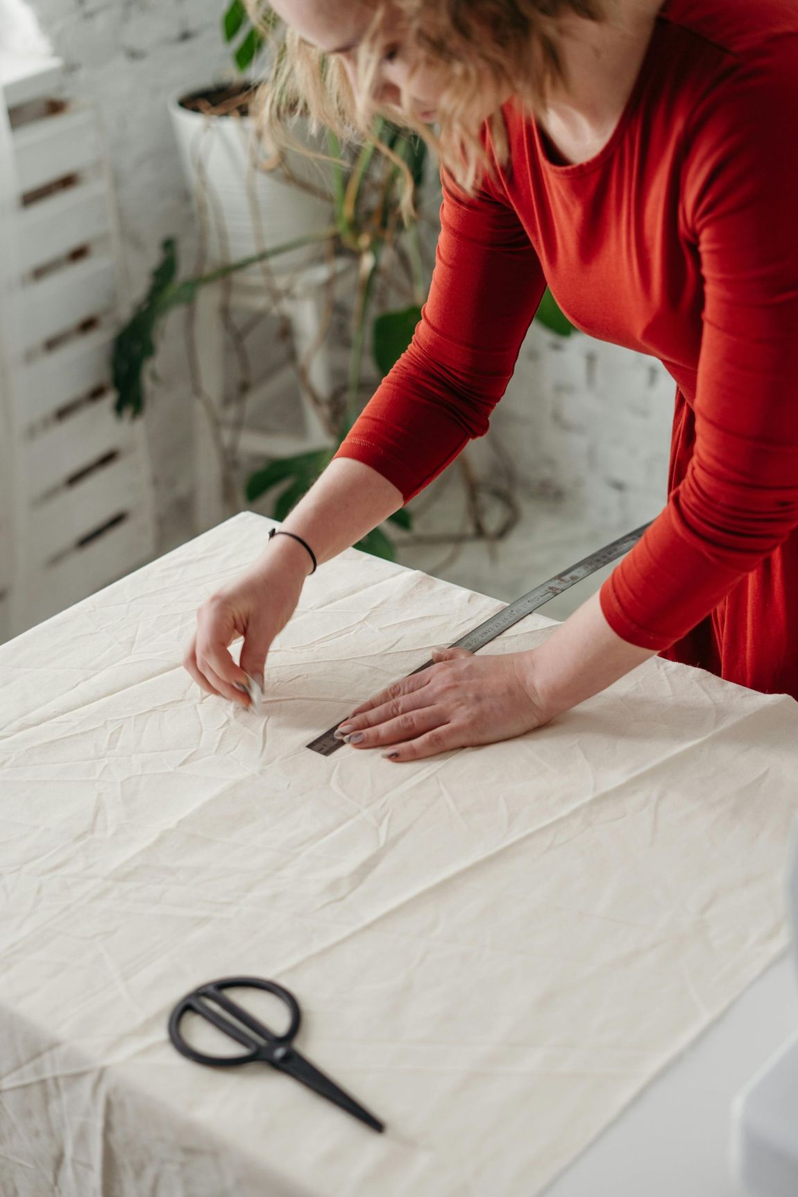 A woman is measuring a piece of fabric with a ruler and scissors.