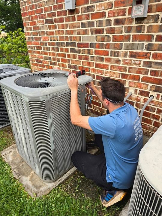 A man is working on an air conditioner outside of a brick building.