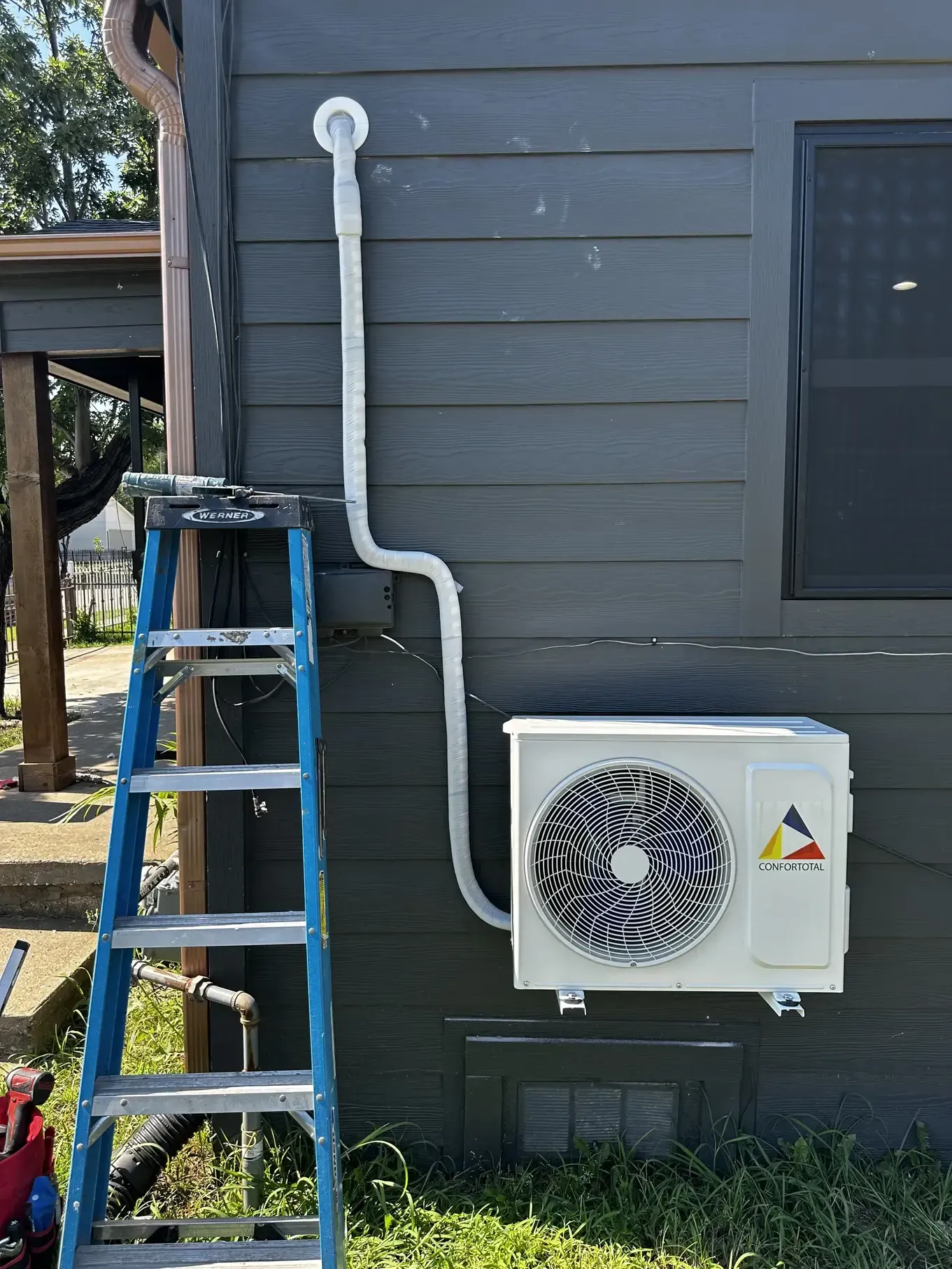A blue ladder is sitting next to a white air conditioner on the side of a house.
