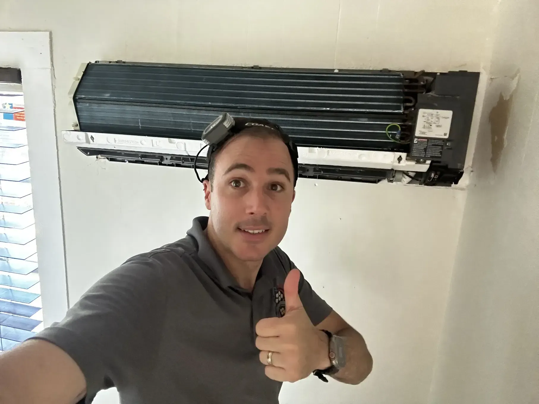A man is giving a thumbs up in front of an air conditioner.