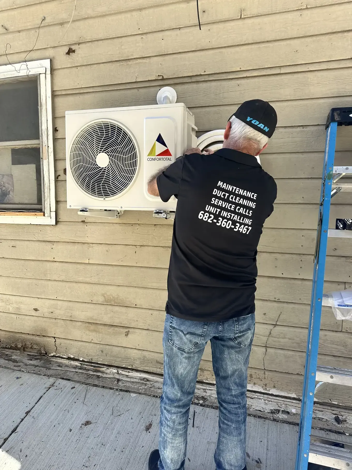A man is installing an air conditioner on the side of a building.