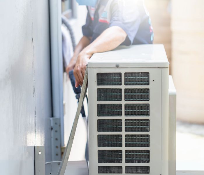 A man is working on an air conditioner outside of a building.