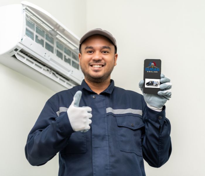 A man is holding a cell phone and giving a thumbs up in front of an air conditioner.