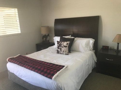 A bedroom with a bed featuring a dark wood headboard, white bedding, a plaid runner, and lamps on matching nightstands.