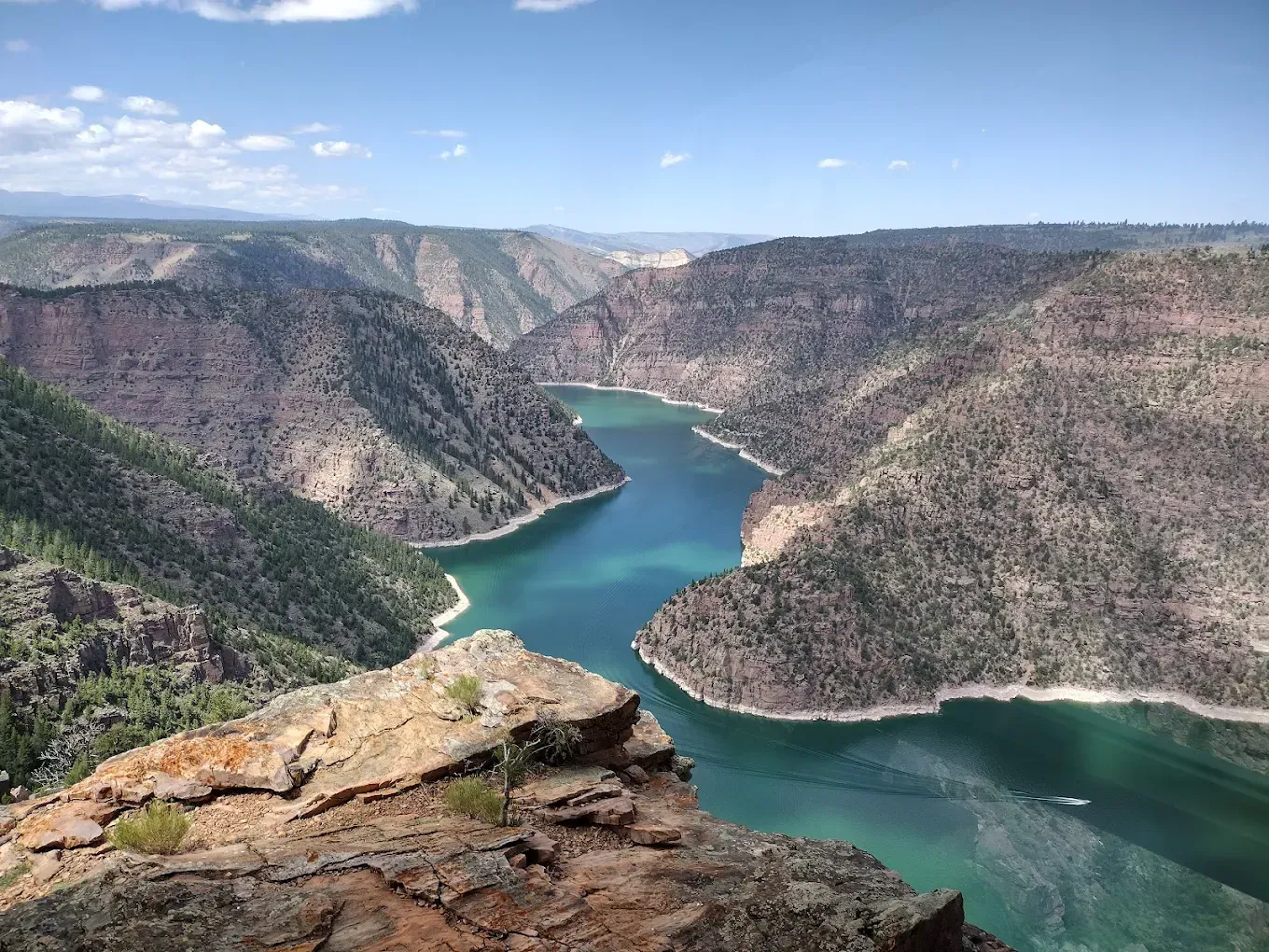 A bright, clear view of a winding turquoise river carved deep into steep, rocky canyon walls under a blue sky.