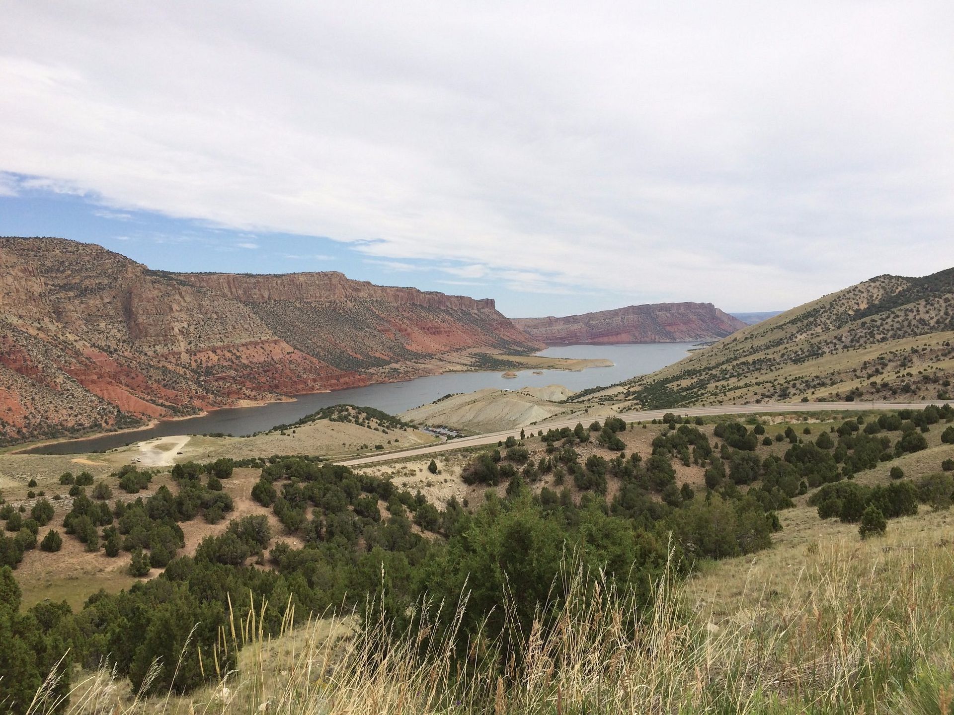 A winding river flows between red-rock canyon walls and grassy, juniper-dotted hills under a cloudy sky.