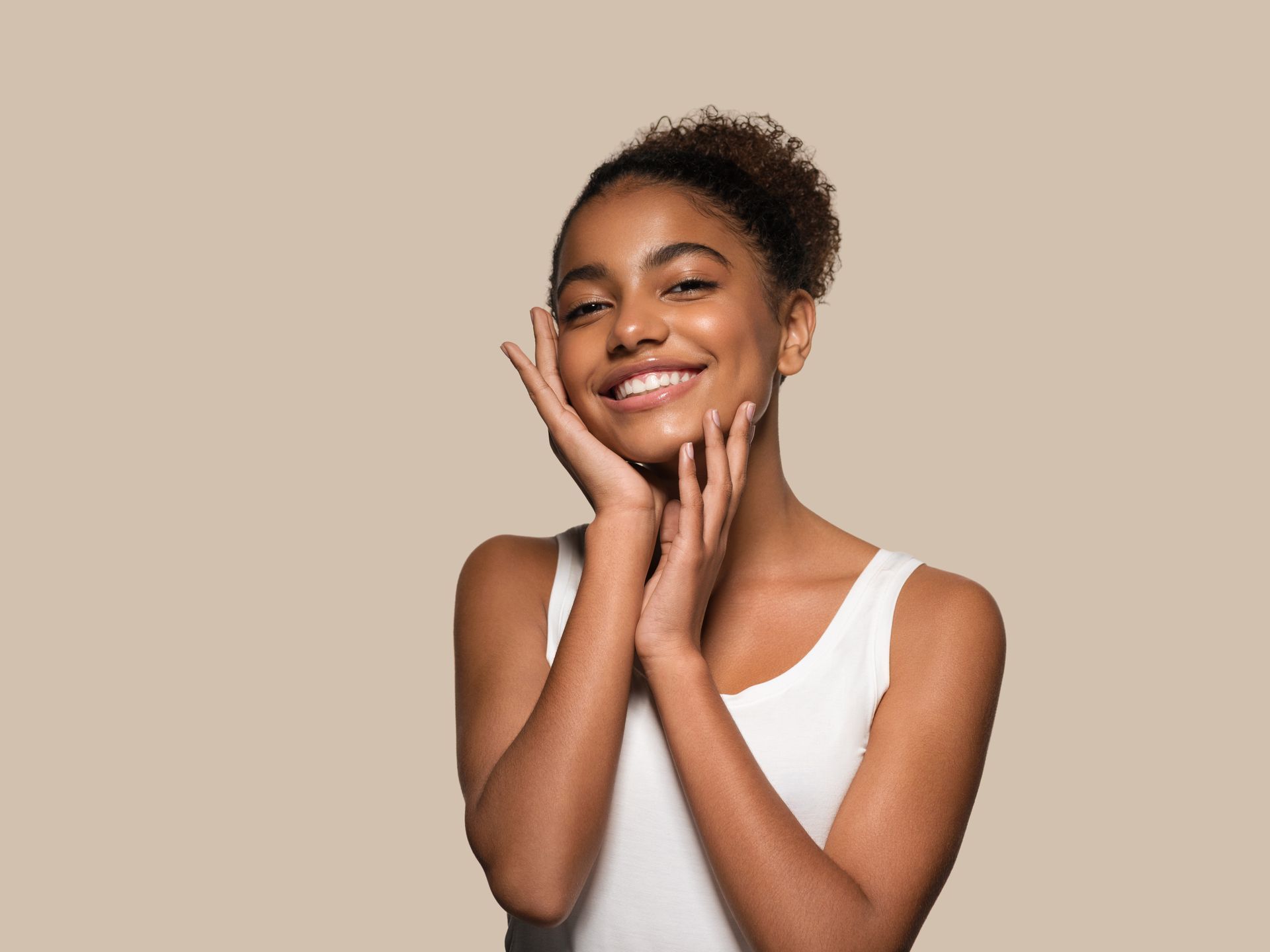 A woman is smiling and touching her face with her hands.