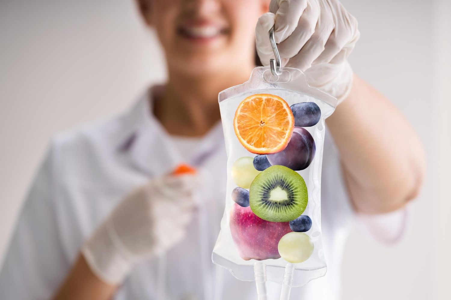 A healthcare worker in gloves holding an IV bag containing a variety of fresh fruits.