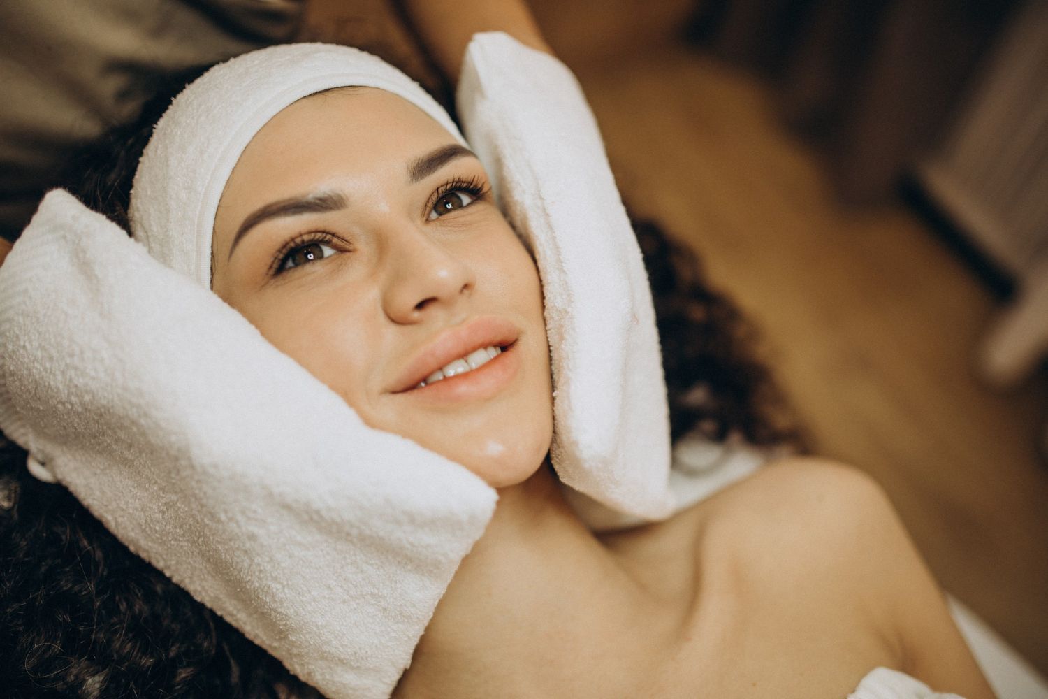 A person lying on a spa bed with soft, white towels wrapped around their head and cheeks during a facial treatment.